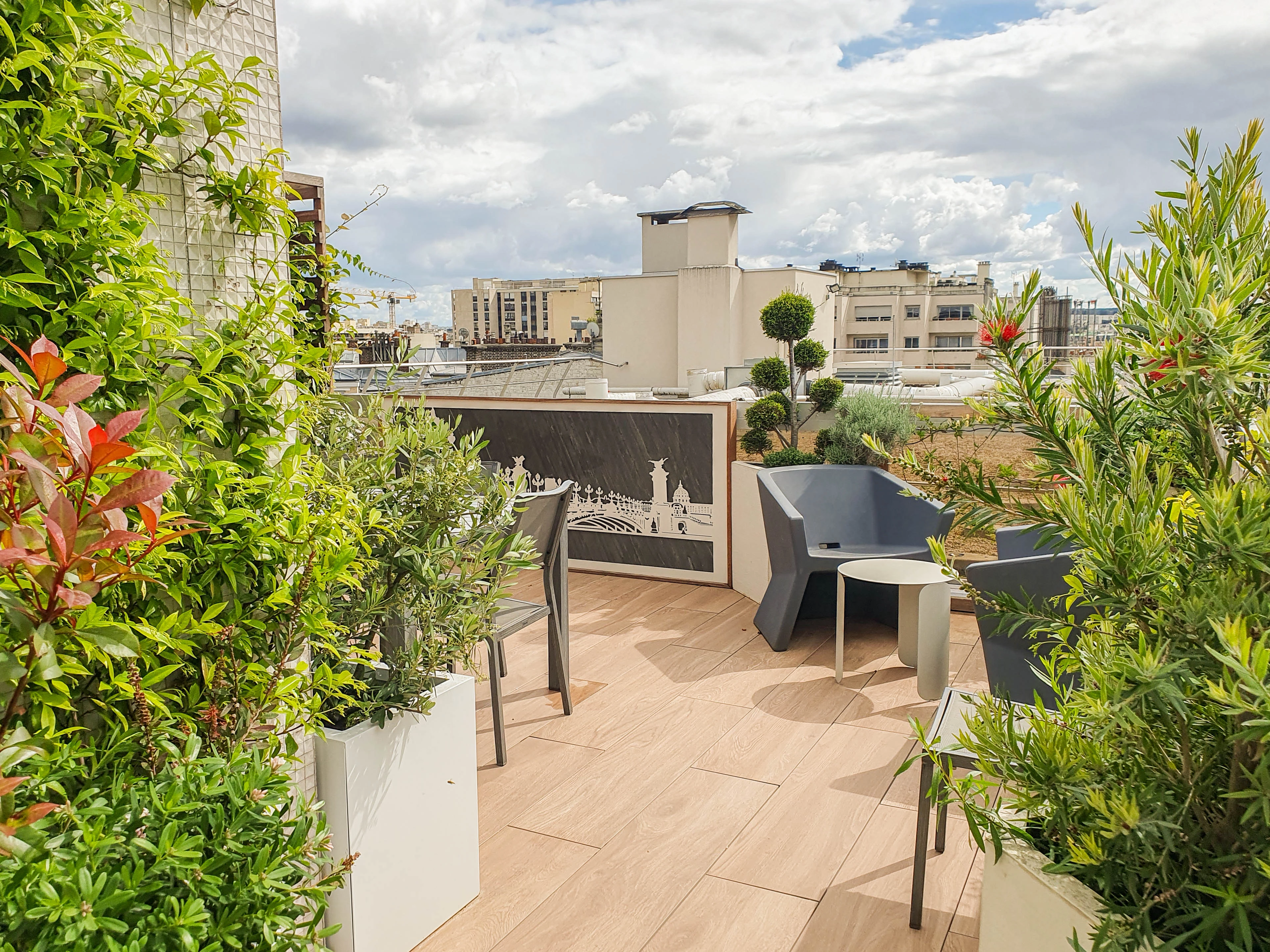 Conception et aménagement d'une grande terrasse comprenant quelques éléments matériels et végétaux structurels forts. La végétalisation dense et variée tend à faire oublier que nous sommes en ville.